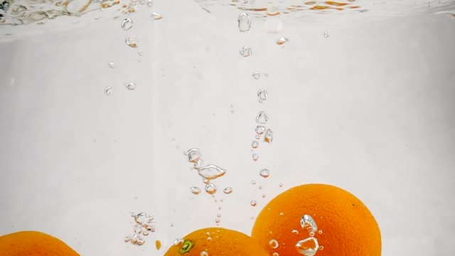 The-orange-falling-in-water-with-bubbles.-Video-in-slow-motion.-Fruits-on-isolated-a-white-background.