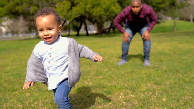 Little-mixed-race-boy-in-park-running-from-father-to-mother