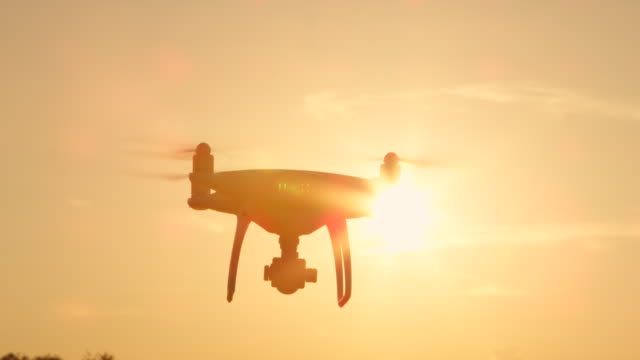 SLOW-MOTION-SILHOUETTE-quadcopter-drone-with-rotating-propellers-flying-over-sun