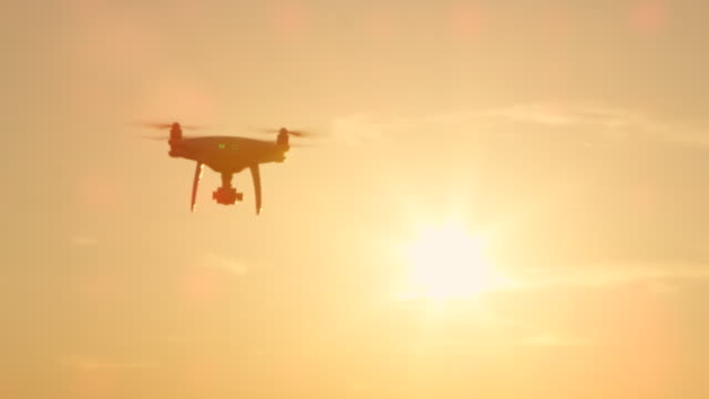 SLOW-MOTION-SILHOUETTE:-Quadcopter-drone-flying-towards-camera-at-golden-sunset