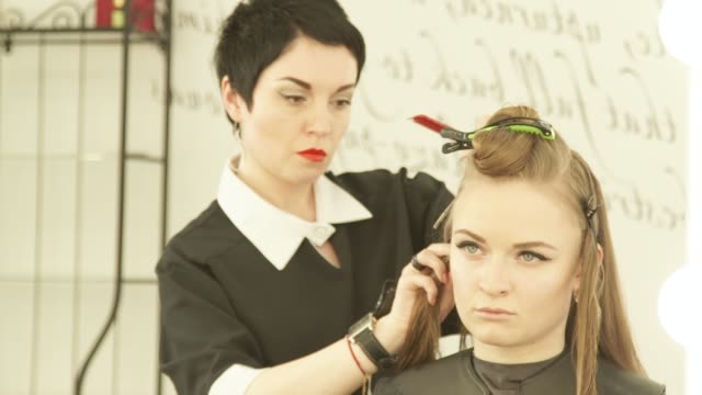 Weibliche-Friseur-mit-Schelle-zur-Befestigung-der-Haare-beim-Friseur-im-Beauty-Salon.-Haircutter-Befestigung-weibliche-Haare-mit-Clip-zum-Haareschneiden-hautnah