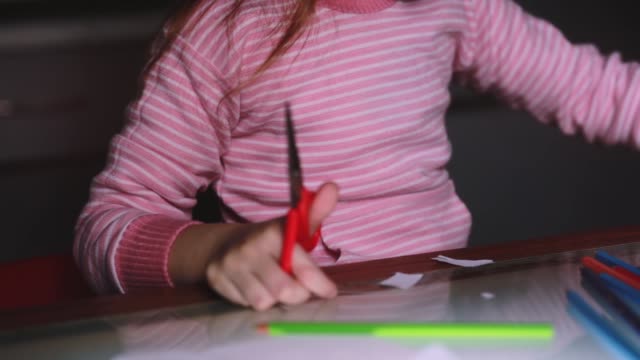 Close-up-shot-of-cute-little-girl's-hands-in-pink-sweater-cutting-paper-shapes-with-scissors-and-drawing-with-a-pencil