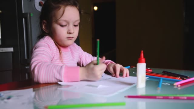Entzückende-kleine-Kaukasische-Mädchen-in-Rosa-Pullover-Zeichnen-von-Formen-mit-einem-Bleistift-auf-einem-Blatt-Papier,-mit-jemandem-sprechen