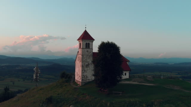 Flying-around-the-old-Catholic-church-on-a-hill-with-a-beautiful-view-of-the-village-in-summertime-in-the-sunset