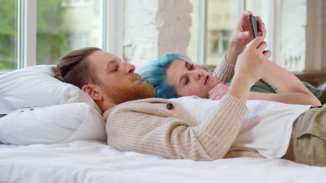 Junges-Paar-mit-Handy-auf-Bett-liegend