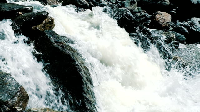 Fast-mountain-stream-flows-out-of-the-glacier-in-the-mountains-close-up.-Water-quickly-flows-through-the-rocks-in-the-wild,-slow-motion.