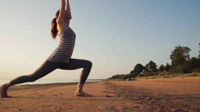Aktive-junge-Frau-Stretching-und-Yoga-am-Strand-bei-Sonnenuntergang-zu-praktizieren.