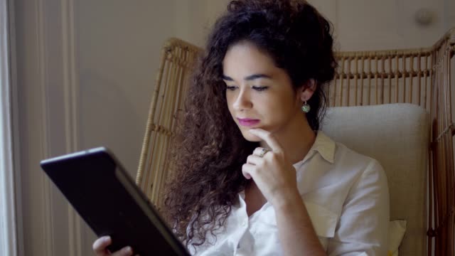 Chica-pensativa-con-el-cabello-rizado-con-tablet-PC-en-el-hogar