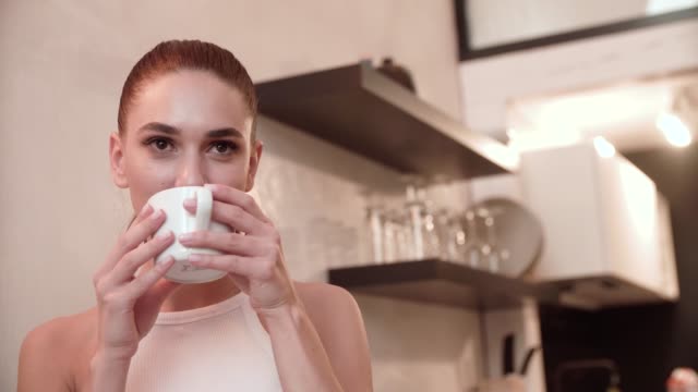 Young-Woman-Drinking-Coffee-In-Kitchen-At-Home