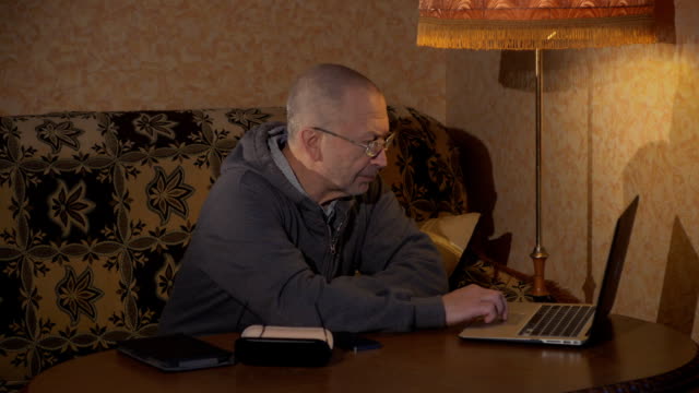 Abuelo-sentado-en-un-escritorio-y-trabajar-en-un-ordenador-portátil.-Está-escribiendo.