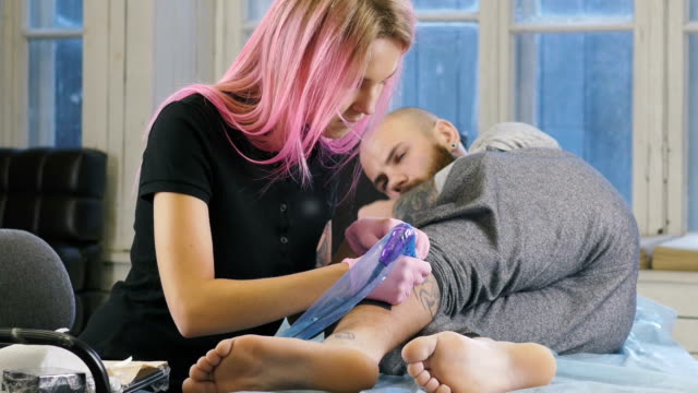 Artista-de-tatuaje-femenino-con-el-pelo-rosa-haciendo-tatuaje-en-el-estudio