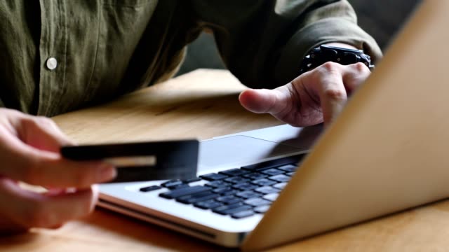 Nahaufnahme-von-männlichen-Händen-halten-Sie-eine-Kreditkarte-und-einen-Laptop-für-den-Online-Einkauf-verwenden.