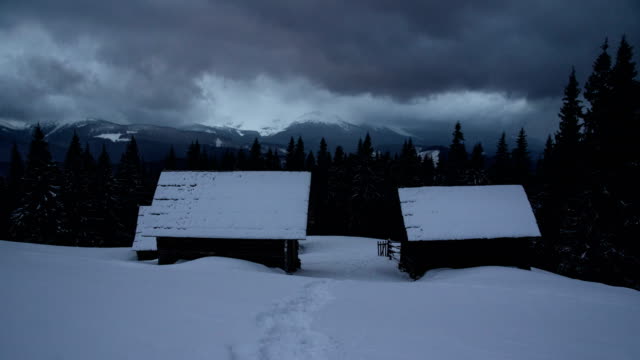 Time-lapse-thunder-clouds-moving-above-winter-mountain-range-house-hut-cabin-dark-pine-forest-foreground-nature-landscape-wanderlust