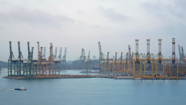 Puerto-de-envío-de-4-K.-Singapur-con-buque-de-carga-navega-lentamente-en-el-mar-y-muchas-grúas-de-contenedor-y-amarillo-en-fondo