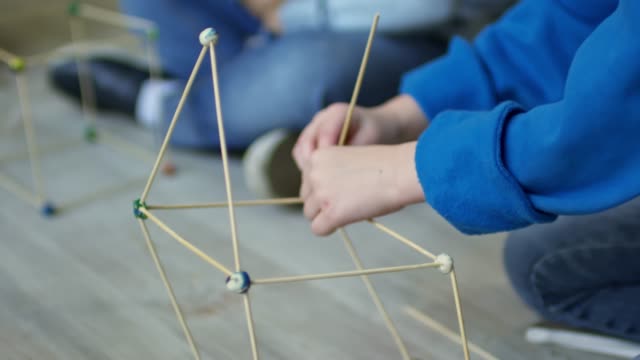 Hands-of-Girl-Constructing-House-Model-with-Wooden-Sticks