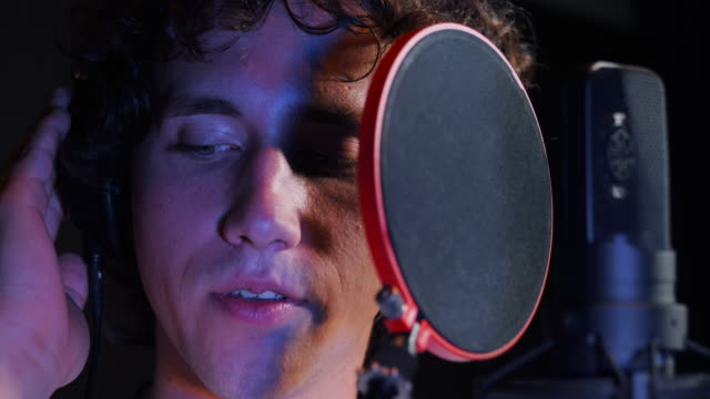 Young-handsome-singer-man-emotionally-writing-song-in-the-studio.-Recording-new-melody-or-album.-Male-vocal-artist-with-curly-hair-singing-alone.-Slow-motion.-4k