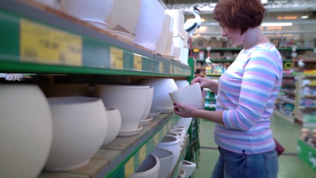 Kaukasischen-Frau-in-der-Nähe-von-Regalen-Keramiktopf-für-Haushalt-im-Shop-auswählen