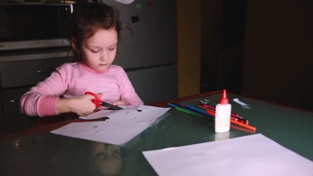 Schöne-kleine-Vorschule-europäischen-Mädchen-im-Rosa-Pullover-sitzen-am-Tisch-zu-Hause-allein-Schnittformen-aus-Papier