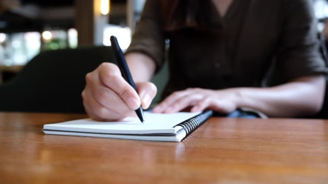 Lenta-de-la-mano-de-una-mujer-escribiendo-en-cuadernos-en-blanco-en-la-mesa-de-madera