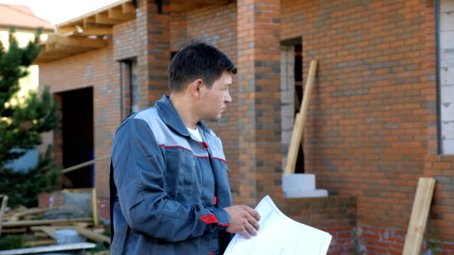Adult-man-looking-at-paper-plans-standing-outdoors-of-building-under-construction,-slow-motion