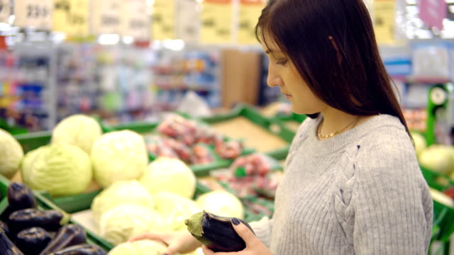 Mujer-joven-en-el-Departamento-de-verdura-de-un-supermercado-elige-berenjenas