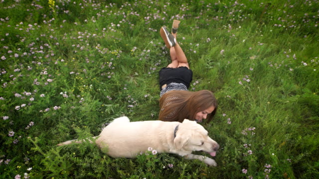 Schöne-Frau-Besitzer-liegen-auf-dem-Rasen,-liebkosen-und-streicheln-ihren-Labrador-Hund