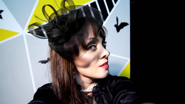 Halloween-party,-night,-frightening-portrait-of-a-woman-with-a-terrible-makeup-in-a-black-witch-suit,-croaks-in-front-of-the-camera