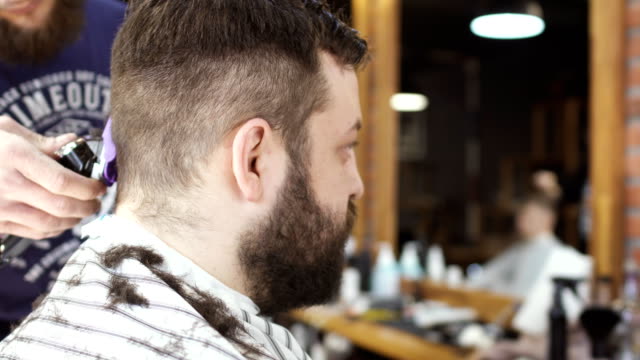 Young-guy-looks-at-mirror-in-barbershop-and-enjoys-new-hairstyle