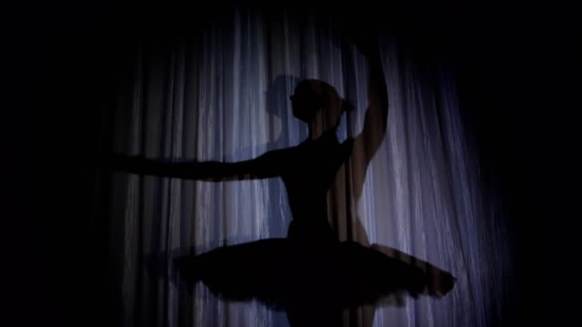 auf-der-Bühne-der-alten-Theater-Halle-gibt-es-eine-Ballerina-tanzen-Schatten-im-Ballett-Tutu-in-Strahlen-der-Scheinwerfer.-Sie-ist-elegant-bestimmte-Bewegung-Ballett-Schwanensee-tanzen.