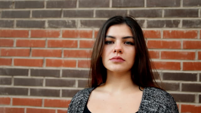 Portrait-of-a-young-confident-woman-against-a-brick-wall.-Slow-motion-shot.