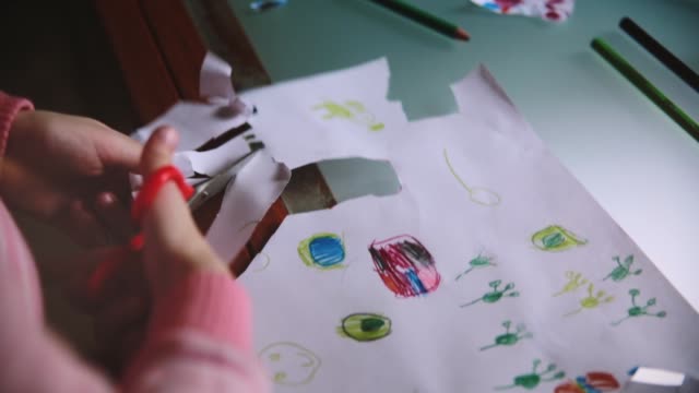 Nahaufnahme-der-niedliche-kleine-Mädchen-Hände-Ausschneiden-handgezeichneten-Bilder-aus-einem-Papierblatt-mit-der-Schere-an-einem-Tisch