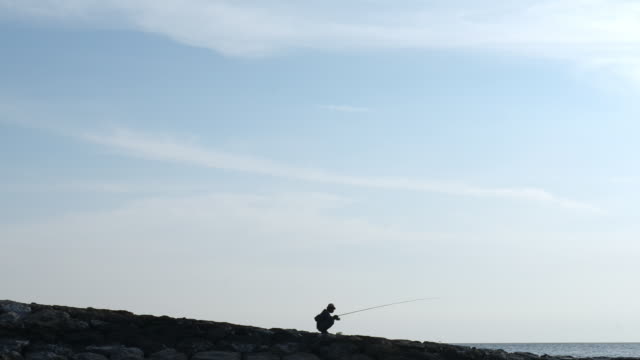 Pescador-sentado-en-dique-en-puesta-del-sol