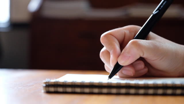 Slow-motion-of-a-woman's-hand-writing-on-blank-notebooks-on-wooden-table