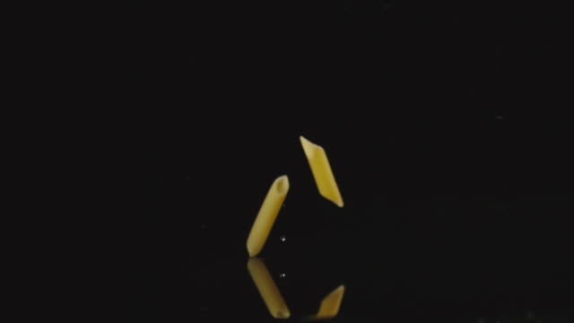 SLOW-MOTION:-Pasta-falls-in-water-in-dark-and-splashes-scatter-in-different-directions