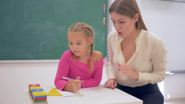 Schule-Vorbereitung,-Lehrerin-Frau-hilft-Lernenden-Mädchen-erwerben-Kenntnisse-über-Kunststoff-Figuren-am-Tisch-in-der-Nähe-Tafel-im-Klassenzimmer-der-Schule