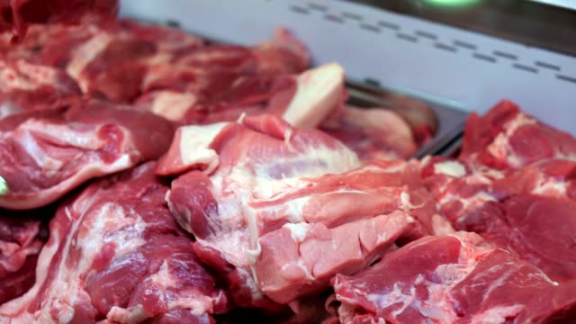 Refrigerator-in-the-store.-A-pile-of-raw-pork-meat.-Hand-butcher-turns-over-pieces-of-meat