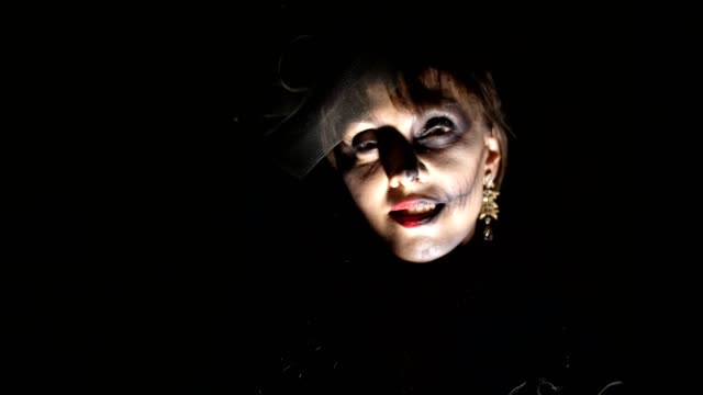 Halloween-Party,-Nacht,-Porträt-einer-Frau-in-der-Dämmerung-in-den-Strahlen-des-Lichtes-erschreckend.-Frau-mit-einem-schrecklichen-Make-up-in-einem-schwarzen-Hexenkostüm