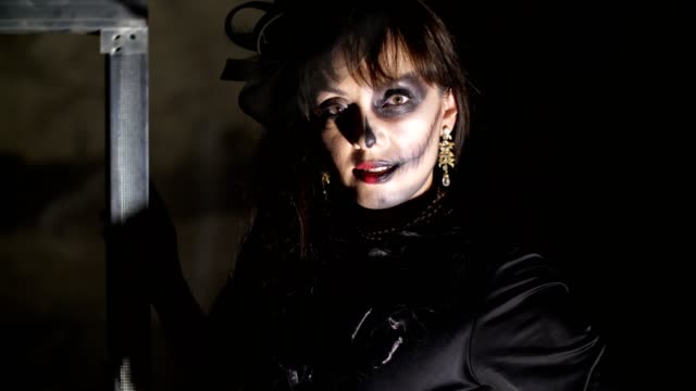 Halloween-party,-night,-frightening-portrait-of-a-woman-in-the-twilight,-in-the-rays-of-light.-woman-with-a-terrible-make-up-in-a-black-witch-costume