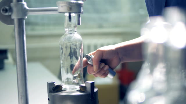 Factory-worker-checks-bottle,-rotating-it-on-a-special-instrument.-4K.