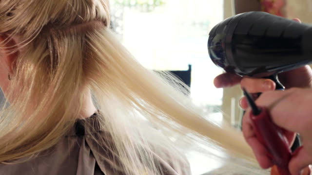 Male-hairdresser-combing-hair-to-blonde-girl-in-beauty-salon,-close-up