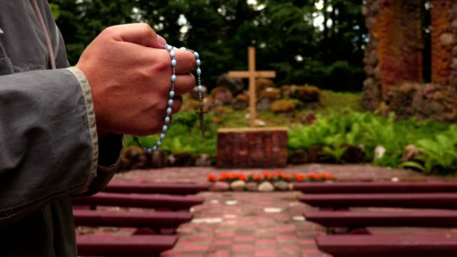 Man-with-rosary-near-cross-at-outdoor