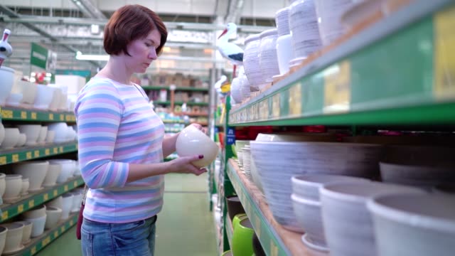 Caucasian-woman-near-shop-shelves-choosing-ceramic-pot-for-household-in-store