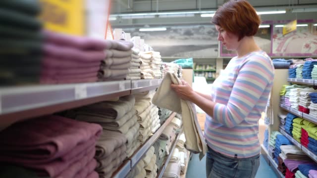 Caucasian-woman-near-shop-shelves-choosing-towel-in-store