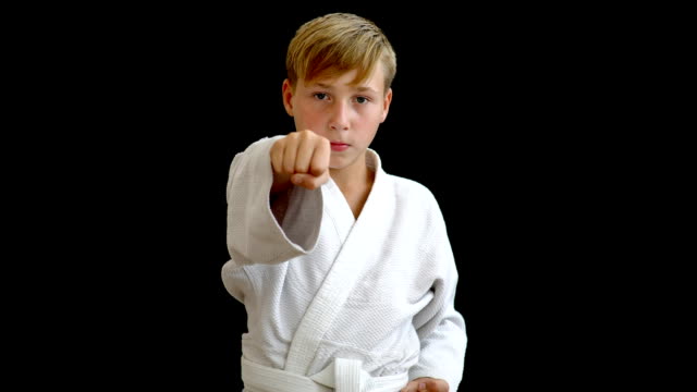 A-young-athlete-in-a-white-kimono-shows-a-punch-with-his-right-hand.-The-boy-holds-one-arm-around-the-waist,-and-the-other-moves-forward.-The-boy-has-blond-hair-and-dark-eyes