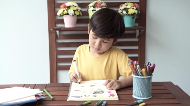 Children-homework.-Young-mixed-race-boy-doing-homework-in-terrace-at-home.-Drawing-and-writing.-Focus-mood.-Back-to-school-concept.