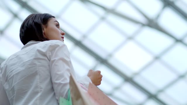 Schöne-junge-Frau-schaut-sich-um-Einkaufszentrum-beim-bewegen-sich-auf-Rolltreppe-mit-Haufen-von-Einkaufstüten-in-der-Hand,-Zeitlupe-erschossen