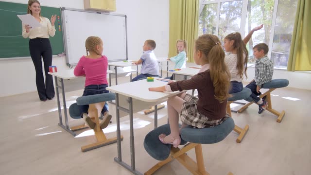school-lesson,-young-teacher-near-board-conducts-cognitive-lesson-for-Smart-children-at-desk-in-classroom-of-school
