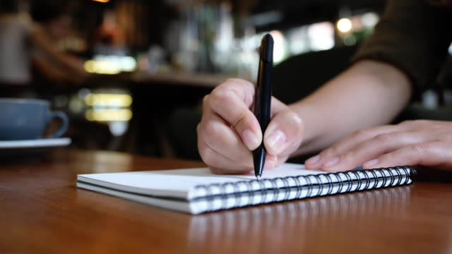 Die-Hand-einer-Frau-schreiben-auf-leere-Notebooks-auf-Holztisch-im-café