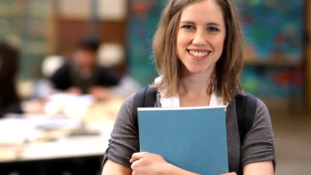 A-college-student-holds-her-books-and-smiles-into-the-camera