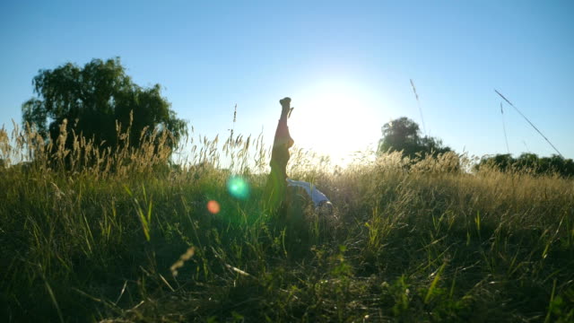 Dolly-shot-of-young-man-practicing-yoga-at-meadow-on-sunny-day.-Athlete-doing-exercise-on-mat-in-grass.-Sporty-guy-training-at-summer-field.-Concept-of-healthy-active-lifestyle.-Slow-motion-Close-up